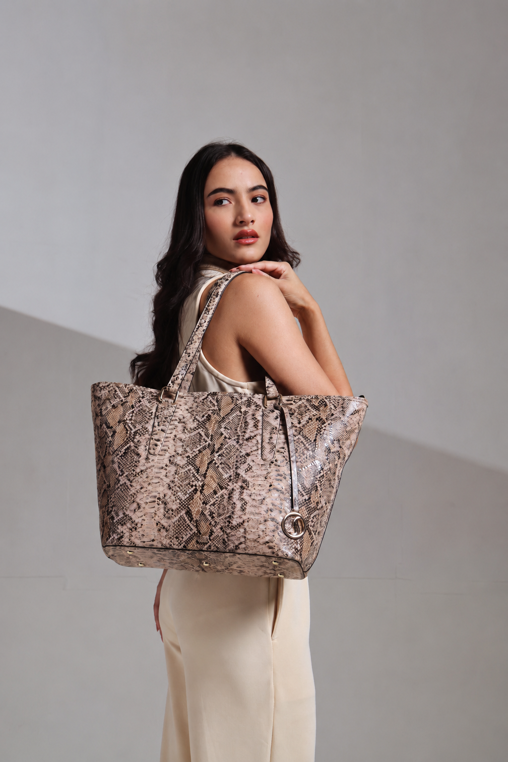 Woman holding a large snakeskin-patterned MASHAK tote bag against a neutral background